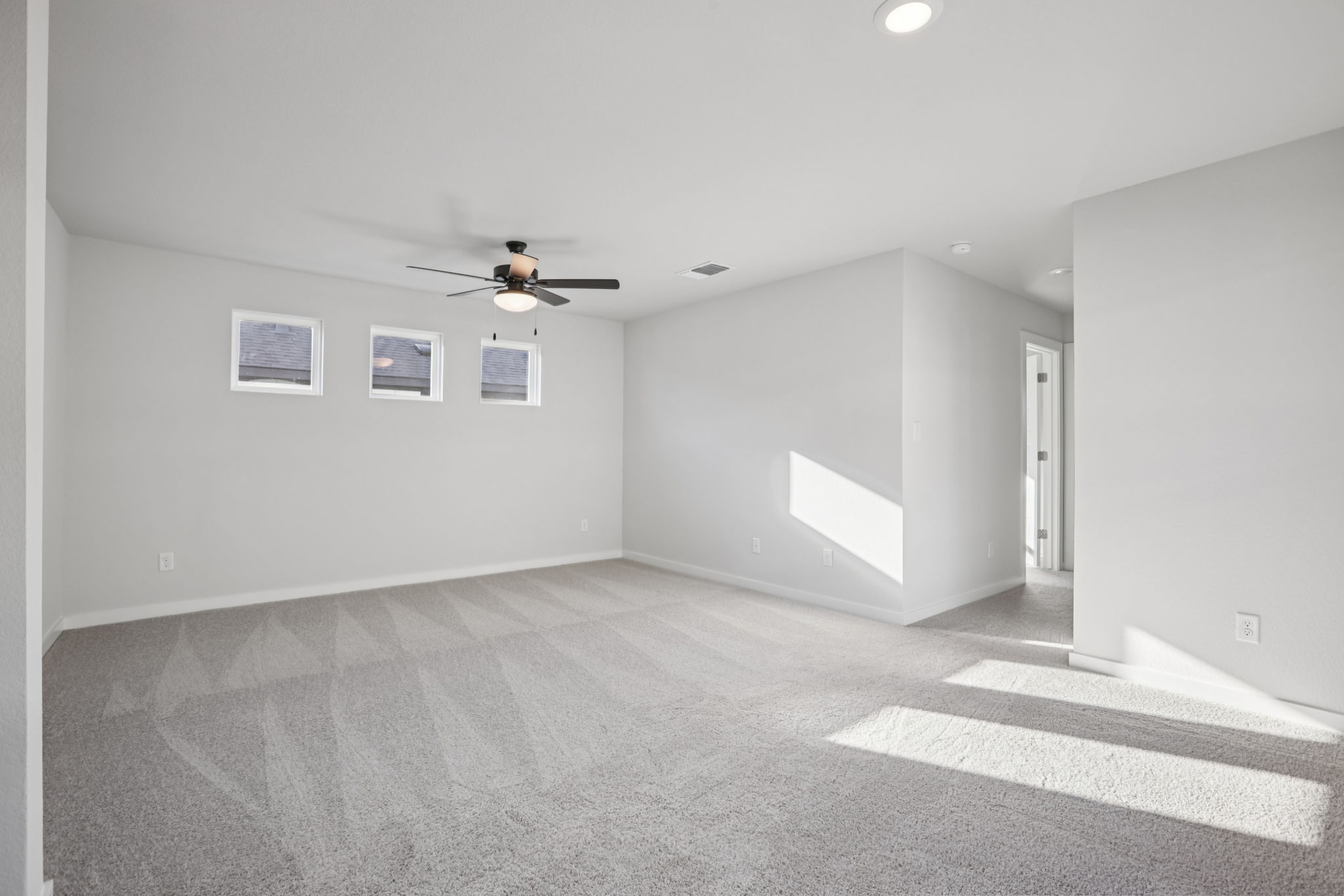 A room with a ceiling fan and a carpet.