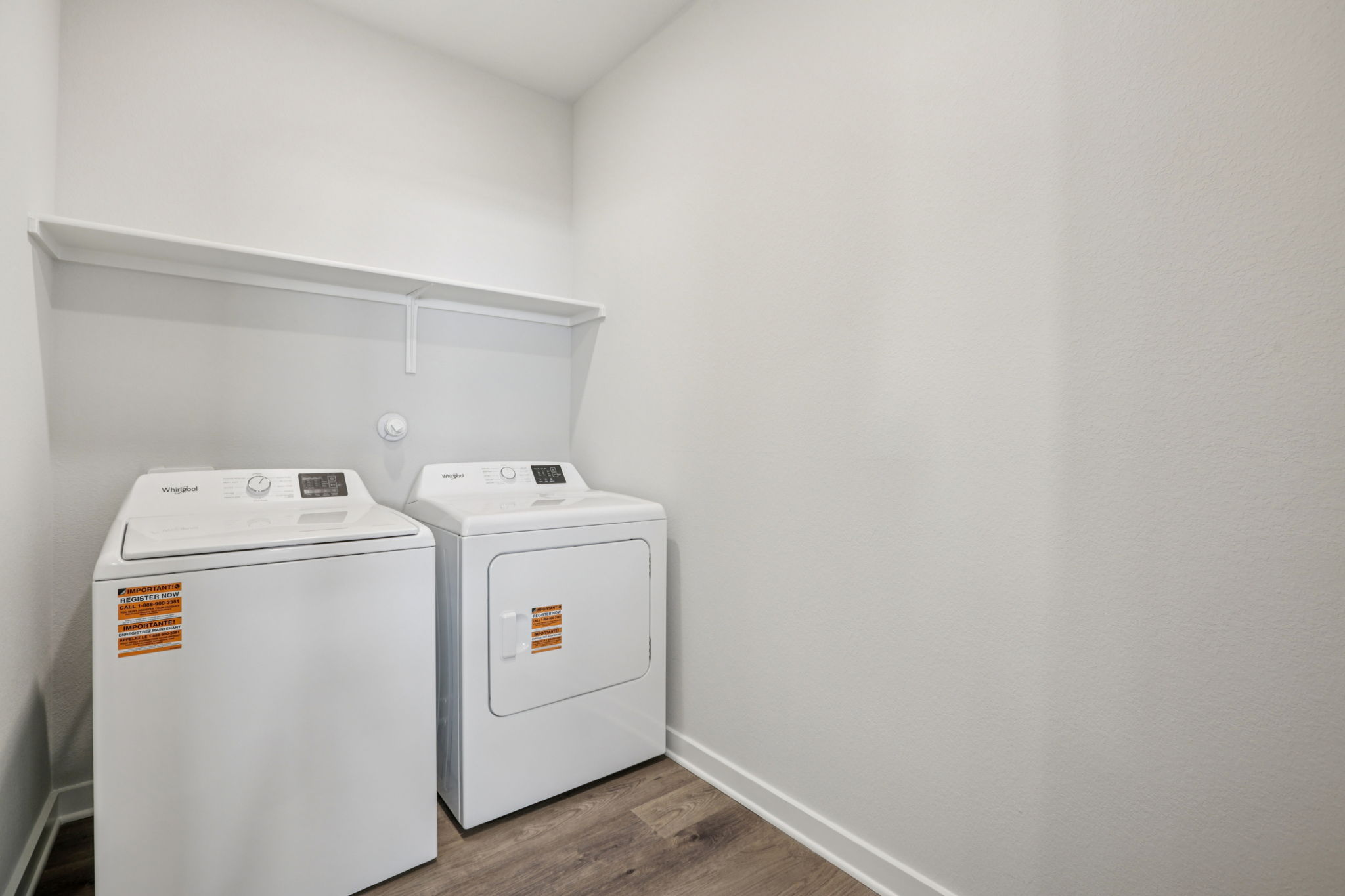 A white laundry room with a white wall and a white shelf.