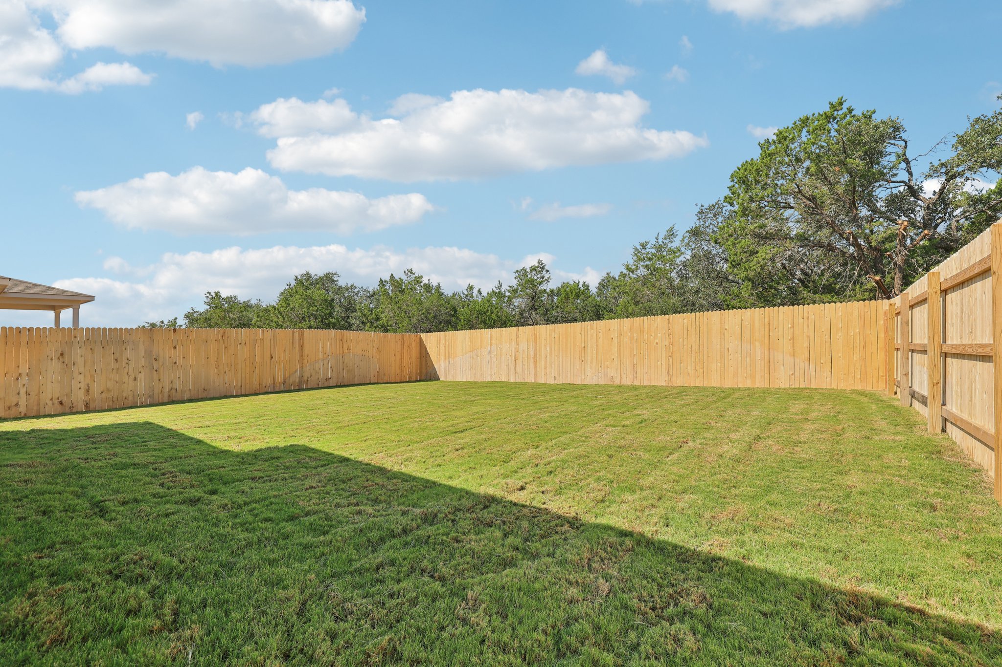 A fenced in yard with a wood fence and trees in the background.