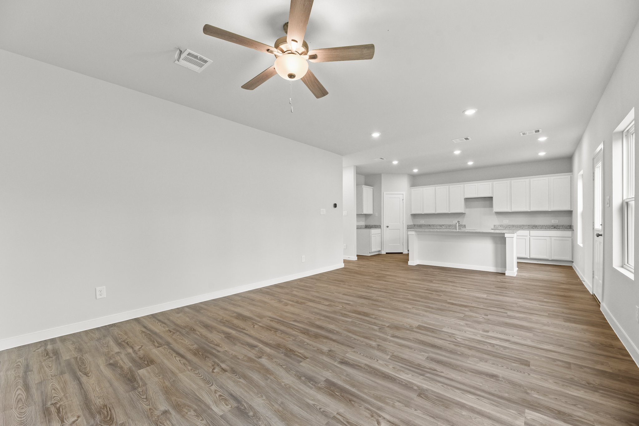A large empty room with a ceiling fan and white cabinets.