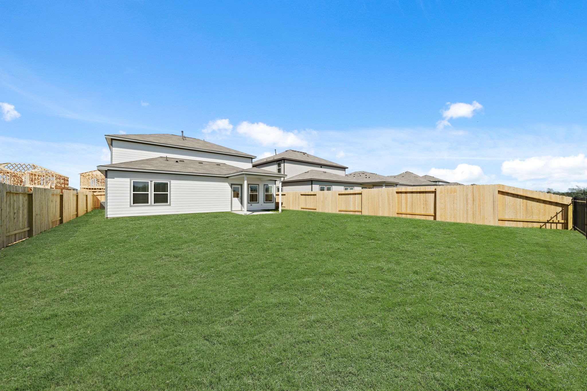 A large green field with a fence and a house in the background.