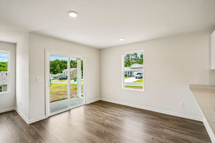 A room with a wood floor and a glass door with a view of a field and trees.